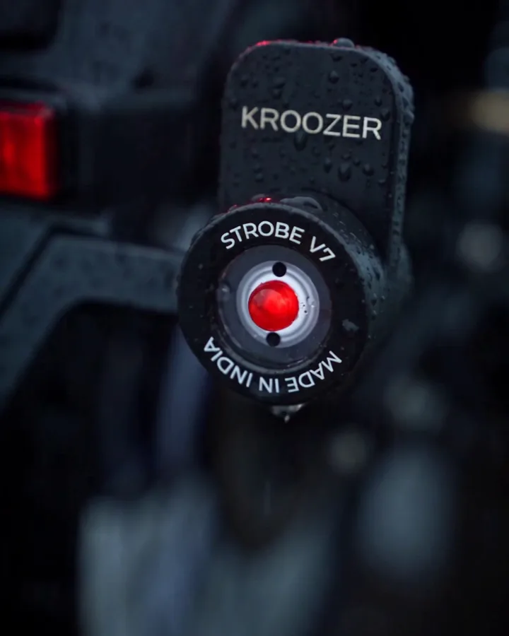 KROOZER Strobe V7.0 pod on its L-bracket at night in the rain, red LED firing, STROBE V7 and MADE IN INDIA marked on the bezel ring