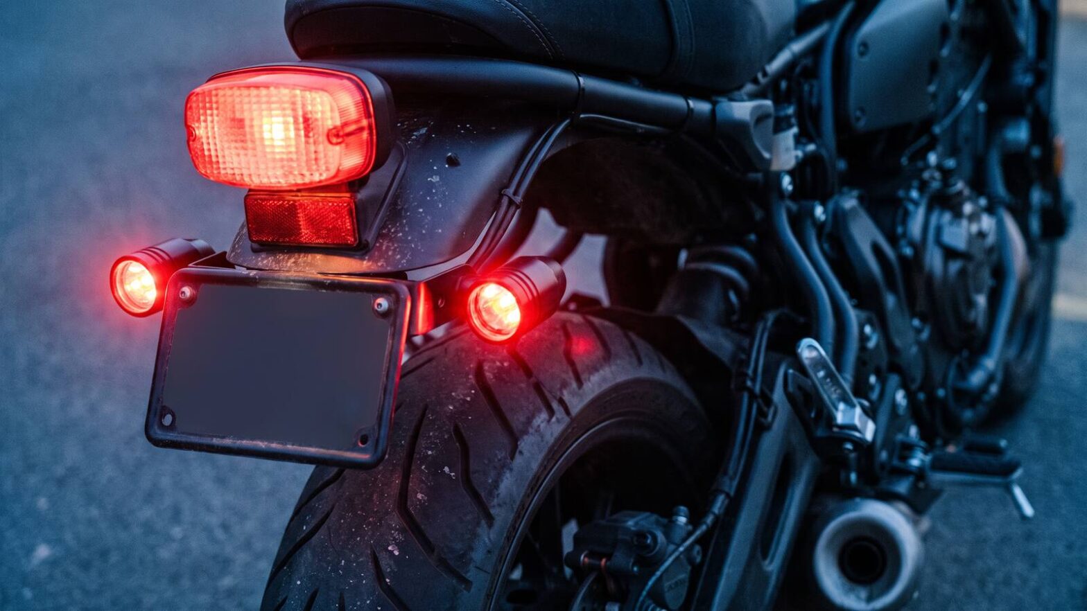 Rear of a motorcycle showing the original tail lamp untouched and two separate red strobe pods flanking the number plate