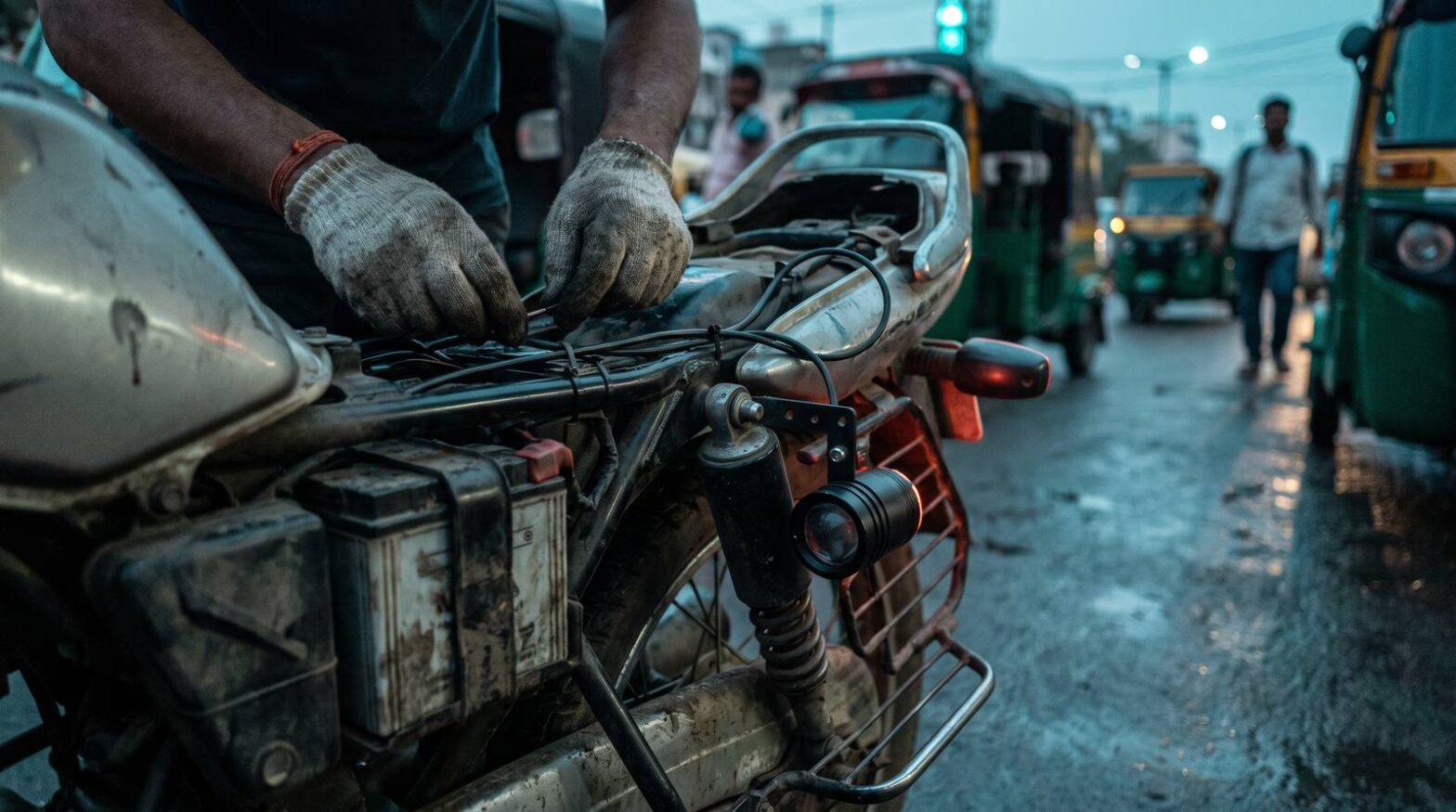 Wiring loom routed along a motorcycle subframe beside the battery box at dusk, with a small black KROOZER strobe pod bolted low near the rear suspension